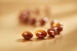 Macro photo of several amber softgel capsules arranged in a line on a beige surface, with shallow depth of field creating a soft, blurred background.